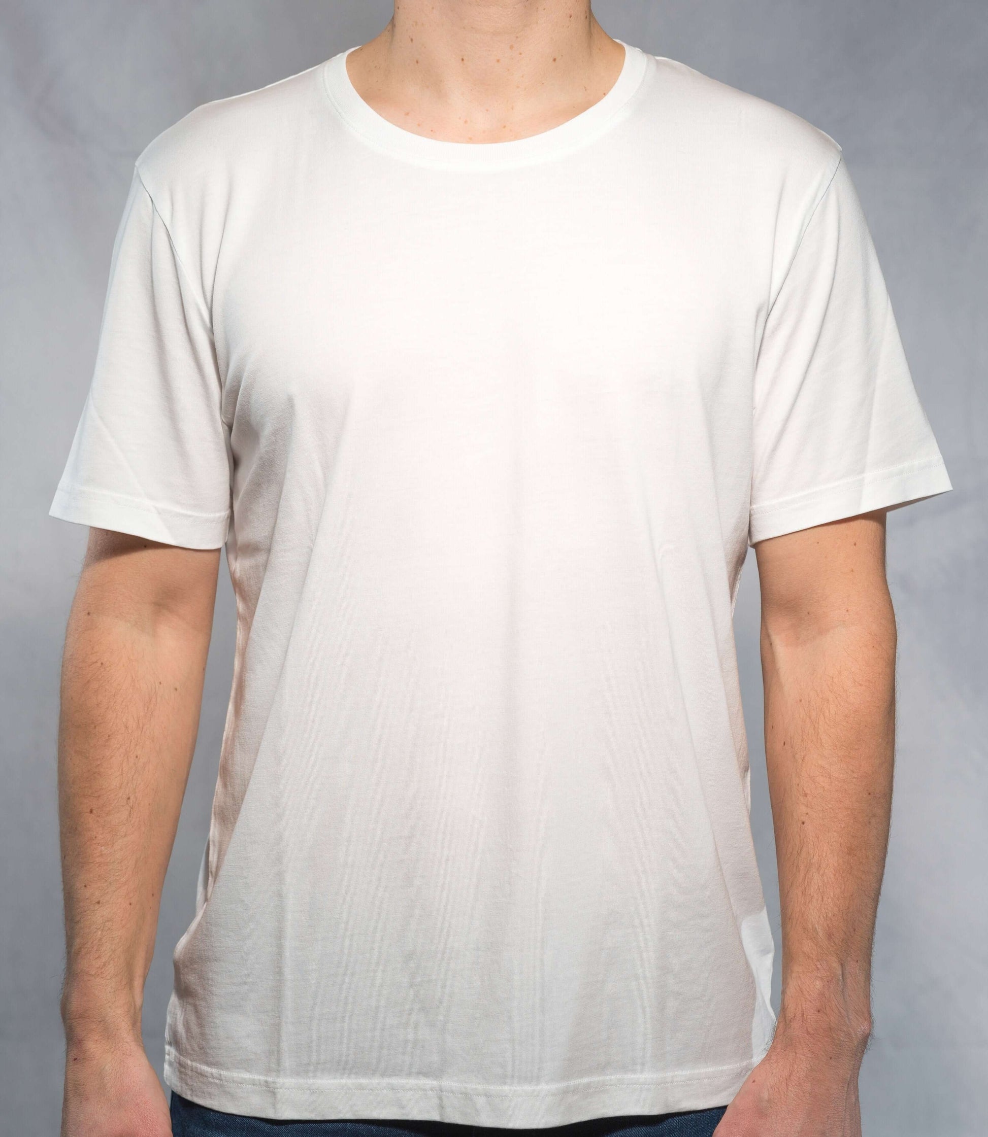 stehender mann mit weißem lyocell shirt von vorne vor einer wand